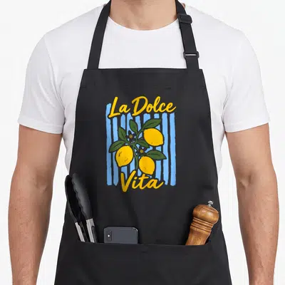 Tablier de cuisine noir avec un motif vintage représentant des citrons jaunes et le texte La Dolce Vita sur un fond de rayures bleues.