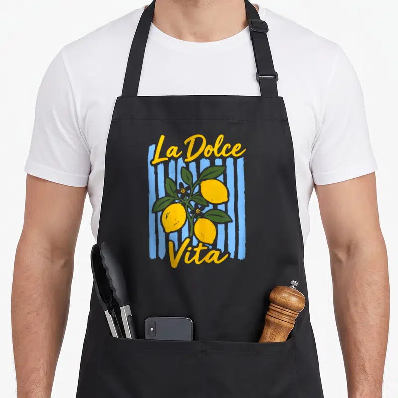 Tablier de cuisine noir avec un motif vintage représentant des citrons jaunes et le texte La Dolce Vita sur un fond de rayures bleues.