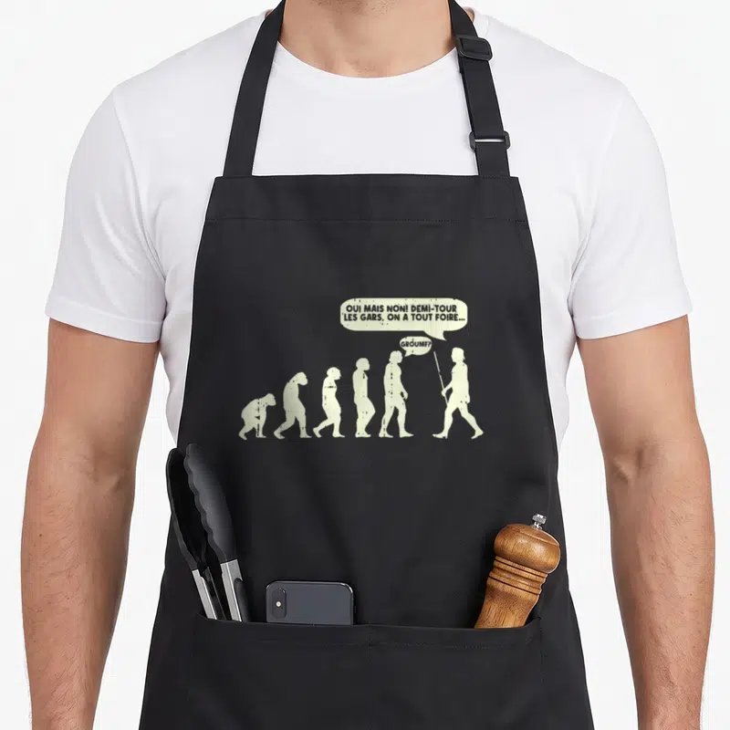 Tablier de cuisine noir avec silhouette évolutive et bulle de dialogue humoristique sur un chemin de randonnée.