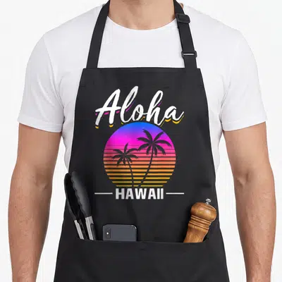 Tablier de cuisine noir avec un soleil rétro Aloha Hawaii orné de palmiers et de texte blanc stylisé.