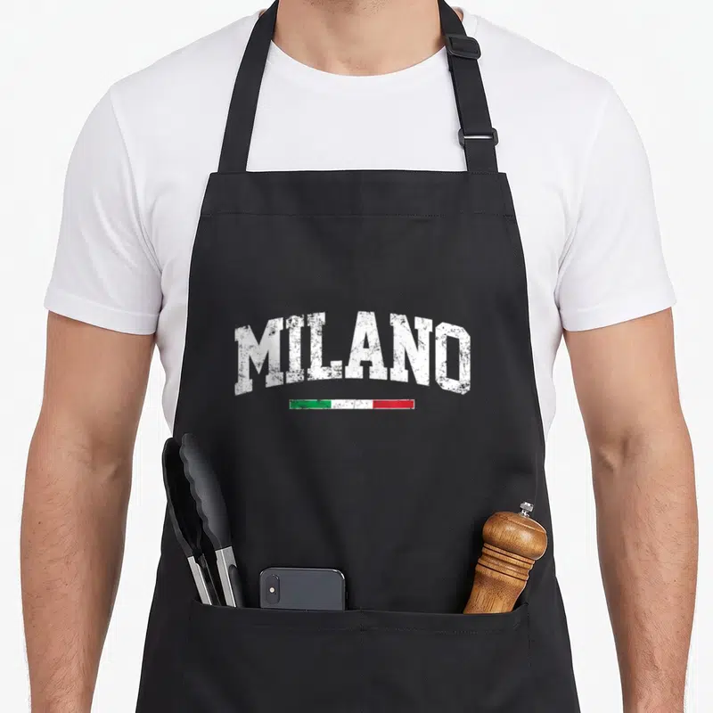 Tablier de cuisine noir avec l'inscription MILANO en lettres blanches usées au-dessus d'une bande aux couleurs vert, blanc et rouge.
