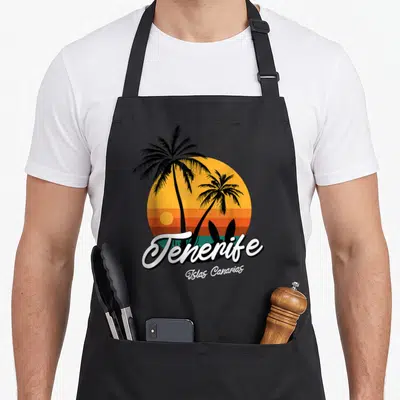 Tablier de cuisine noir avec illustration de palmiers, soleil orange et texte Tenerife Islas Canaries en blanc.