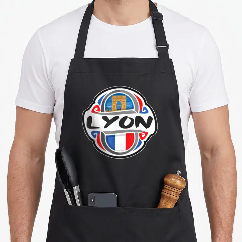 Tablier de cuisine noir avec logo circulaire LYON, Arc de Triomphe et drapeau français stylisé.