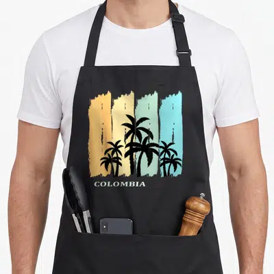 Tablier de cuisine noir avec silhouettes de palmiers et inscription COLOMBIA sur bandes de couleur pastel.