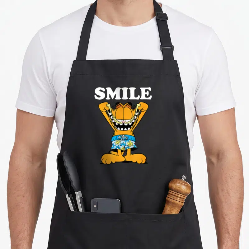 Tablier de cuisine noir avec illustration de Garfield en maillot de bain tirant sur sa bouche avec le texte SMILE au-dessus.