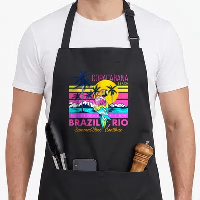 Tablier de cuisine noir avec un perroquet coloré devant un soleil jaune et des palmiers sur fond de plage tropicale.
