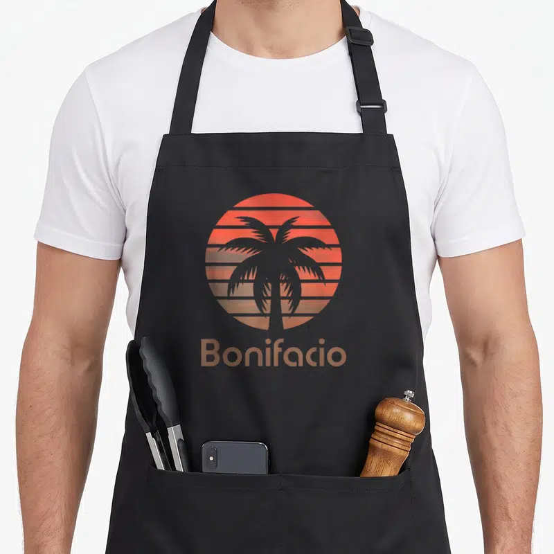 Tablier de cuisine noir avec un soleil orange strié, une palme grise et le texte Bonifacio en bas.
