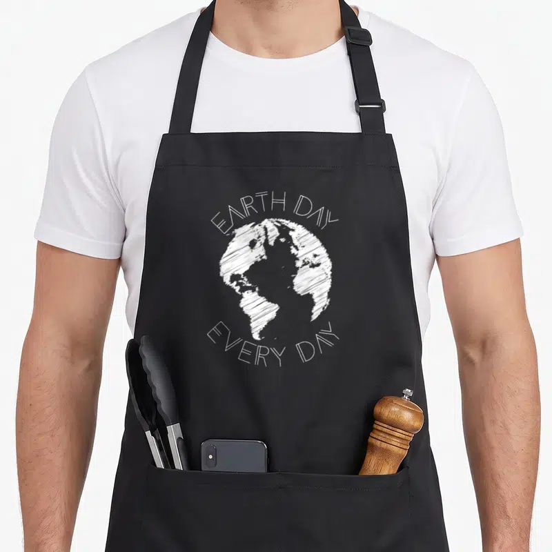 Tablier de cuisine noir avec illustration blanche d'une planète esquissée et le texte Earth Day Every Day.
