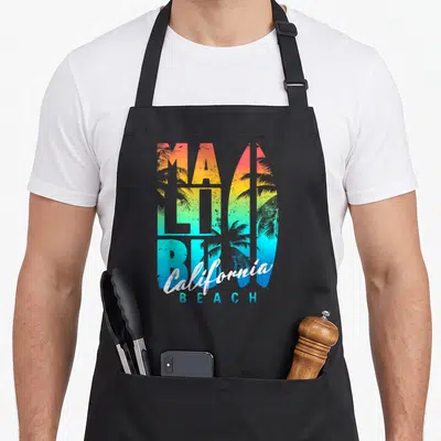 Tablier de cuisine noir avec typographie colorée Malibu et silhouette de planche de surf aux palmiers intégrés.