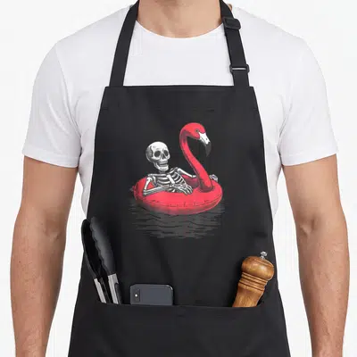 Tablier de cuisine noir avec une tête de mort s'amusant dans un gonflable flamant rose rouge sur l'eau.