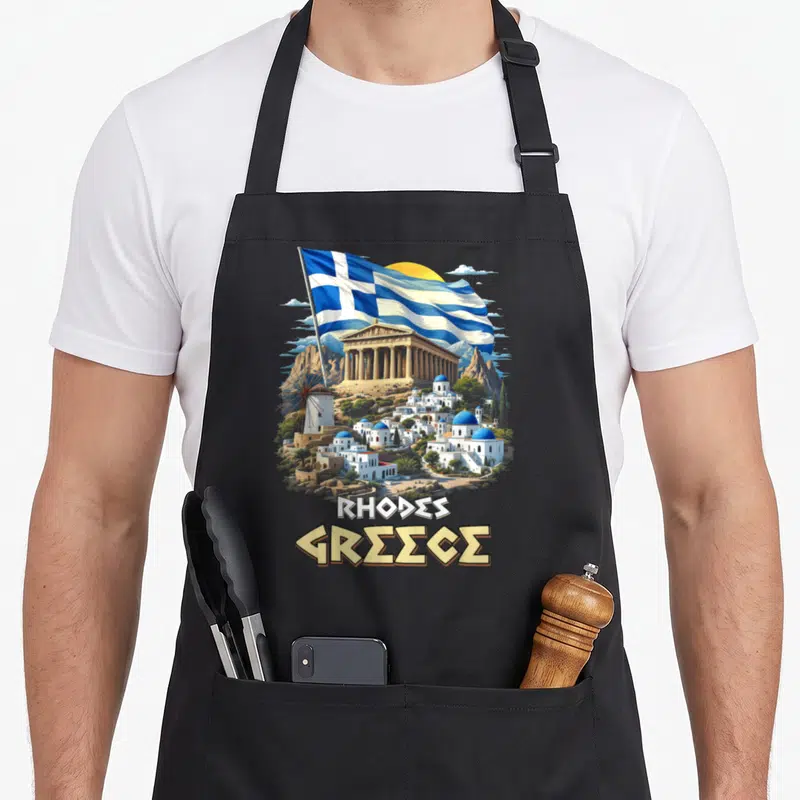 Tablier de cuisine noir avec illustration du drapeau de la Grèce, un temple antique et un village aux dômes bleus sur fond de soleil.