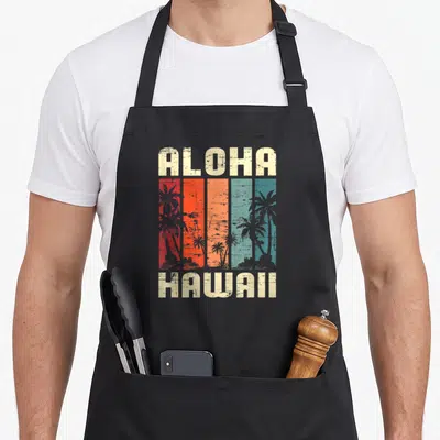 Tablier de cuisine noir avec inscription Aloha Hawaii et silhouettes de palmiers sur fond de bandes colorées vintage.