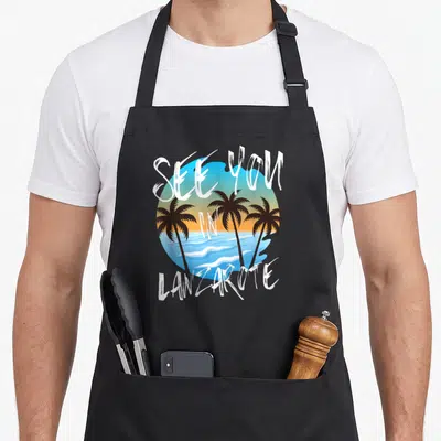 Tablier de cuisine noir avec illustration de palmiers et texte See You In Lanzarote sur fond de soleil couchant.