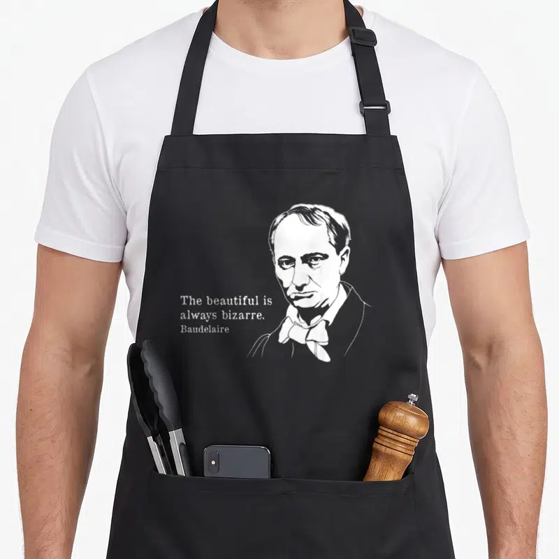 Tablier de cuisine noir avec portrait de Baudelaire et texte « The beautiful is always bizarre » imprimé en blanc.