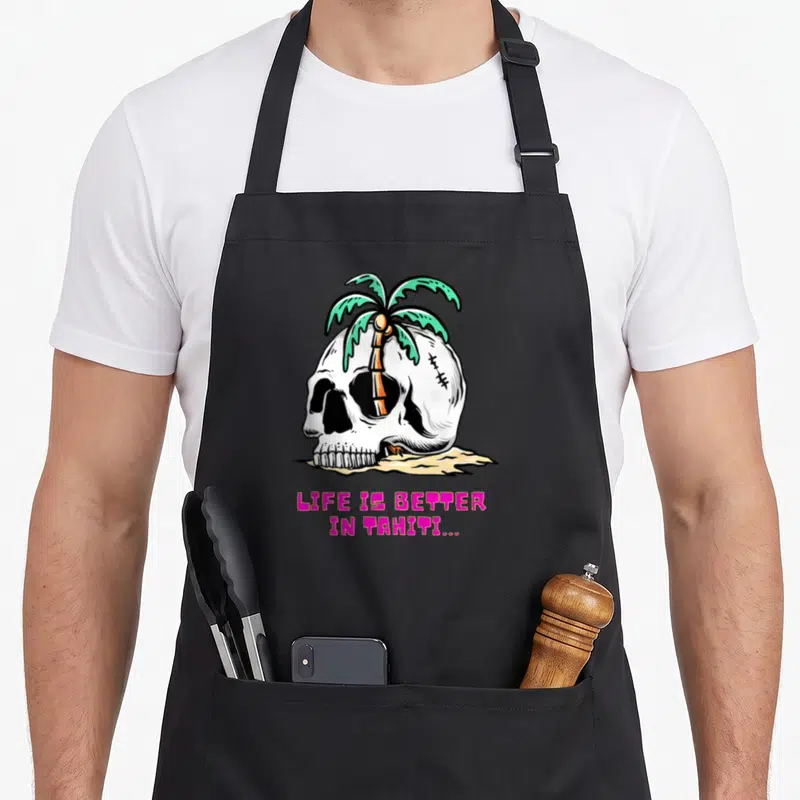 Tablier de cuisine noir avec une tête de mort blanche et un palmier vert sur fond de sable jaune.