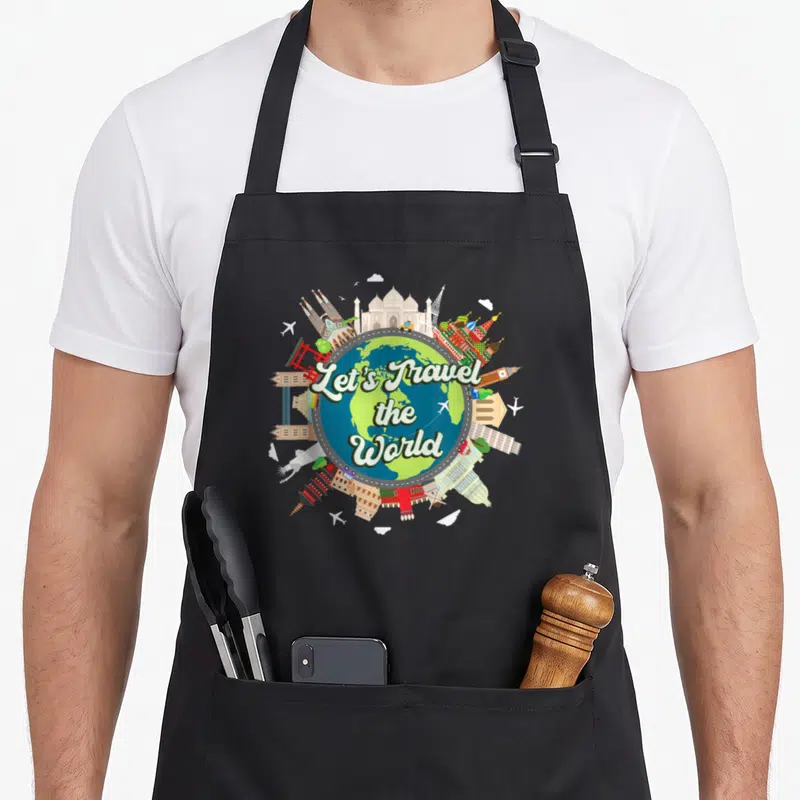 Tablier de cuisine noir avec globe terrestre et monuments internationaux autour du texte Let's Travel the World.