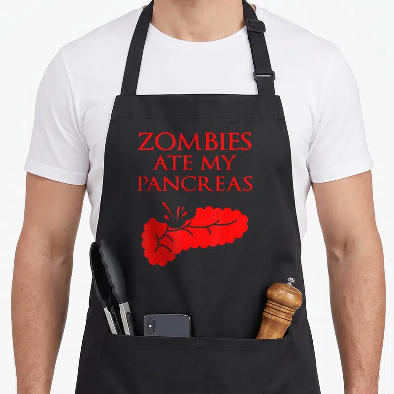 Tablier de cuisine noir avec texte rouge Zombies ate my pancreas et illustration d'organe stylisé en dessous.