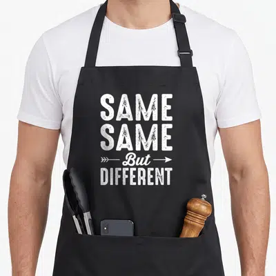 Tablier de cuisine noir avec le texte blanc Same Same But Different et des flèches directionnelles.