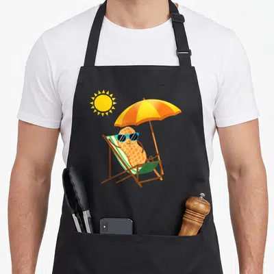 Tablier de cuisine noir avec une noix de cacahuete portant des lunettes de soleil sur un fauteuil de plage sous un soleil