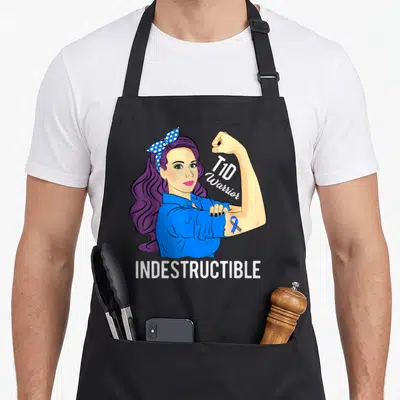 Tablier de cuisine noir avec une femme aux cheveux violets montrant son biceps et le texte T1D Warrior Indestructible