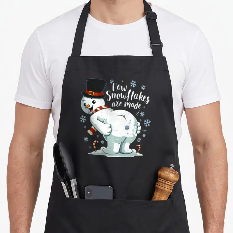 Tablier de cuisine noir avec un bonhomme de neige dos nu et le texte How Snowflakes are made entouré de flocons.