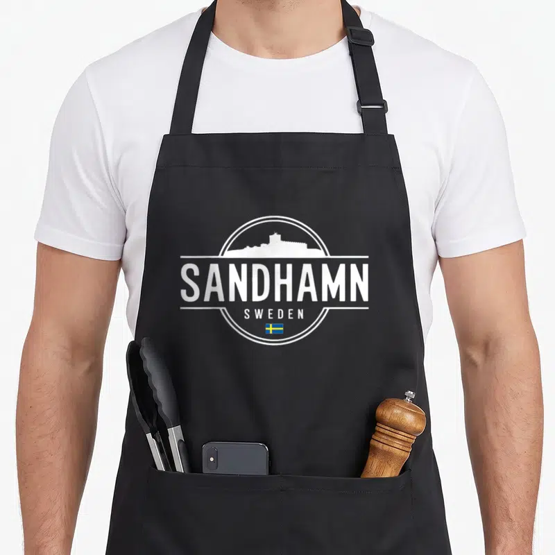 Tablier de cuisine noir avec logo blanc Sandhamn Sweden et petit drapeau suédois en bas du motif circulaire.