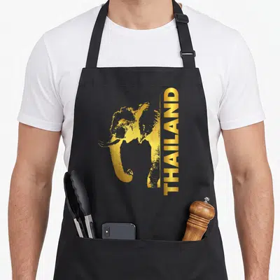 Tablier de cuisine noir avec silhouette d'éléphant dorée et texte vertical THAILAND à côté.
