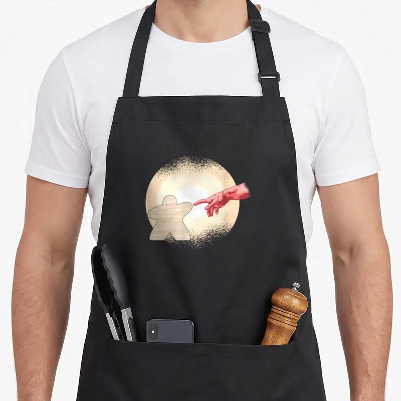 Tablier de cuisine noir avec illustration d'une main rouge touchant un pion de jeu de société en bois sur fond circulaire lumineux.