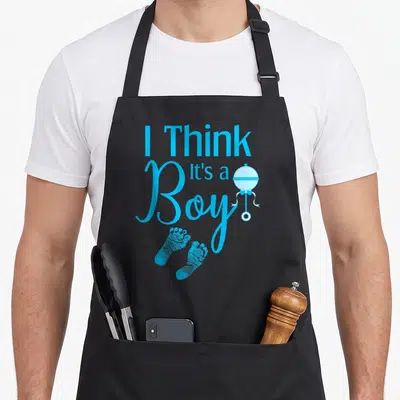 Tablier de cuisine noir avec texte bleu I Think Its a Boy, petits pieds et doudou suspendu.