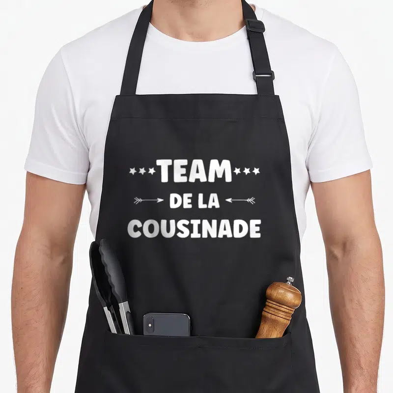 Tablier de cuisine noir avec l'inscription blanche Team de la Cousinade entourée d'étoiles et de flèches.