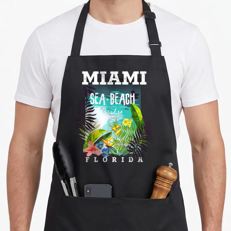 Tablier de cuisine noir avec illustration florale tropicale et texte Miami Sea Beach Paradise Florida.