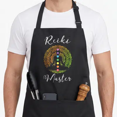 Tablier de cuisine noir avec silhouette de méditant, sept chakras colorés et texte Reiki Master sur fond de mandala.