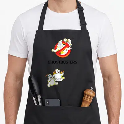Tablier de cuisine noir avec logo fantôme barré rouge, texte GHOSTBUSTERS et deux Stay Puft enflammés souriants.