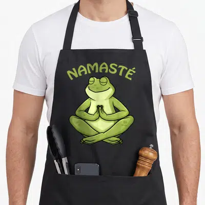 Tablier de cuisine noir avec une grenouille verte assise en tailleur et le texte Namasté en vert clair.