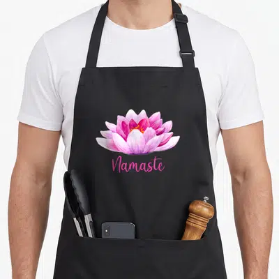 Tablier de cuisine noir avec une fleur de lotus rose et l'inscription Namaste en dessous.