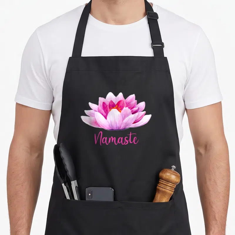 Tablier de cuisine noir avec une fleur de lotus rose et l'inscription Namaste en dessous.