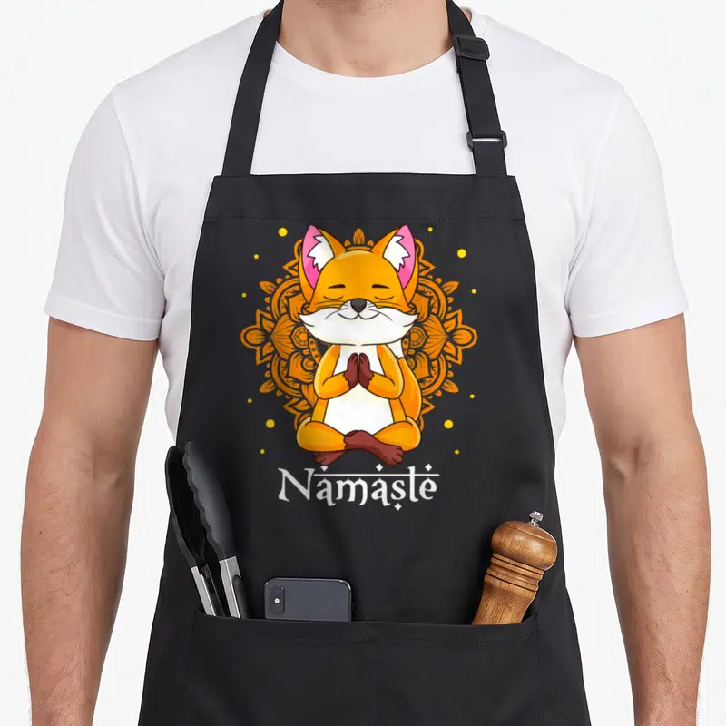 Tablier de cuisine noir avec un renard orange assis en tailleur, les yeux fermés et les mains jointes devant un mandala orange.