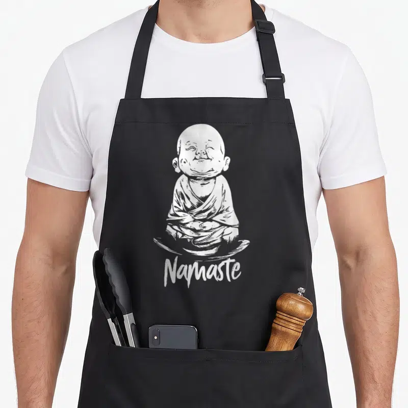 Tablier de cuisine noir avec un petit Bouddha rieur assis en tailleur et l'inscription Namaste en bas.