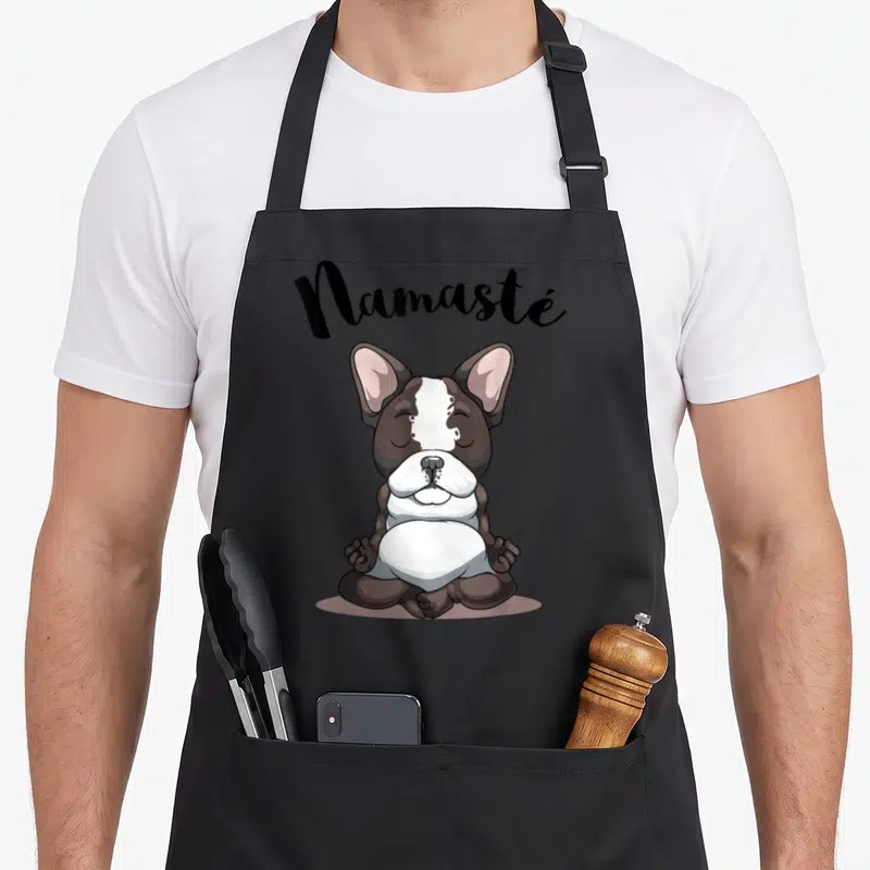 Tablier de cuisine noir avec illustration d'un Bouledogue Français assis en tailleur et le mot Namasté au-dessus.