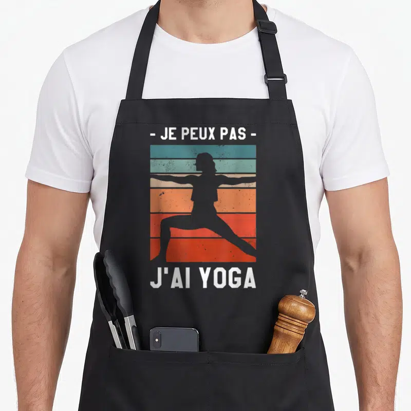 Tablier de cuisine noir avec silhouette de yoga et texte blanc sur fond de bandes colorées vintage orange et bleu.