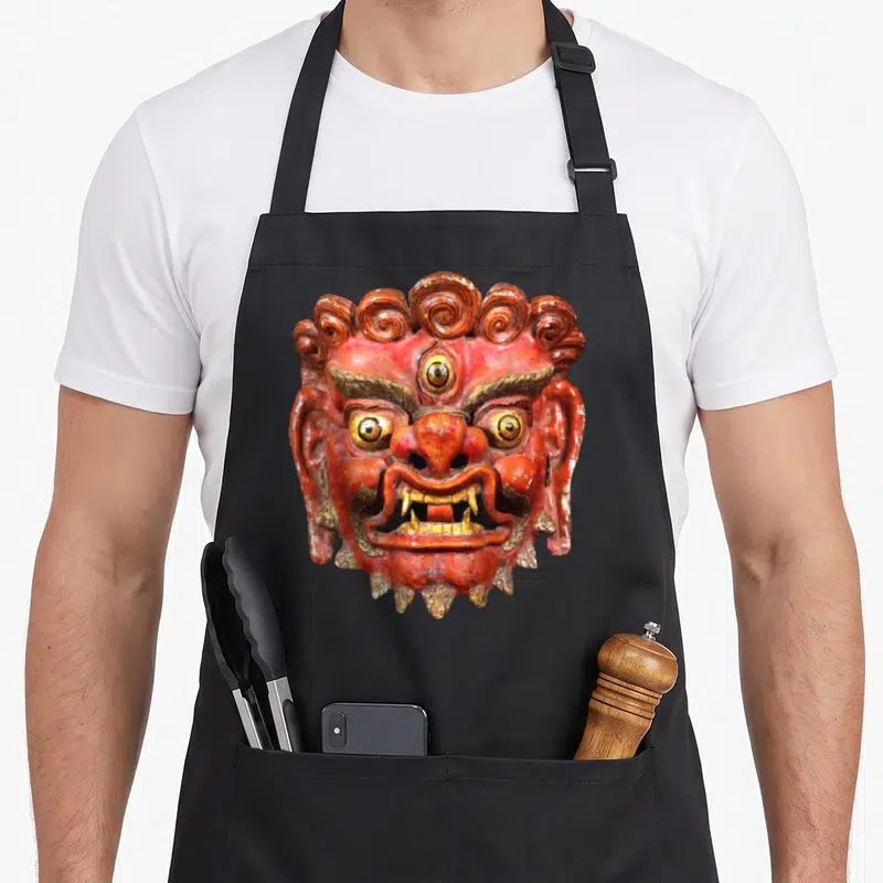 Tablier de cuisine noir avec illustration détaillée d'un masque rouge et doré de style tibétain.