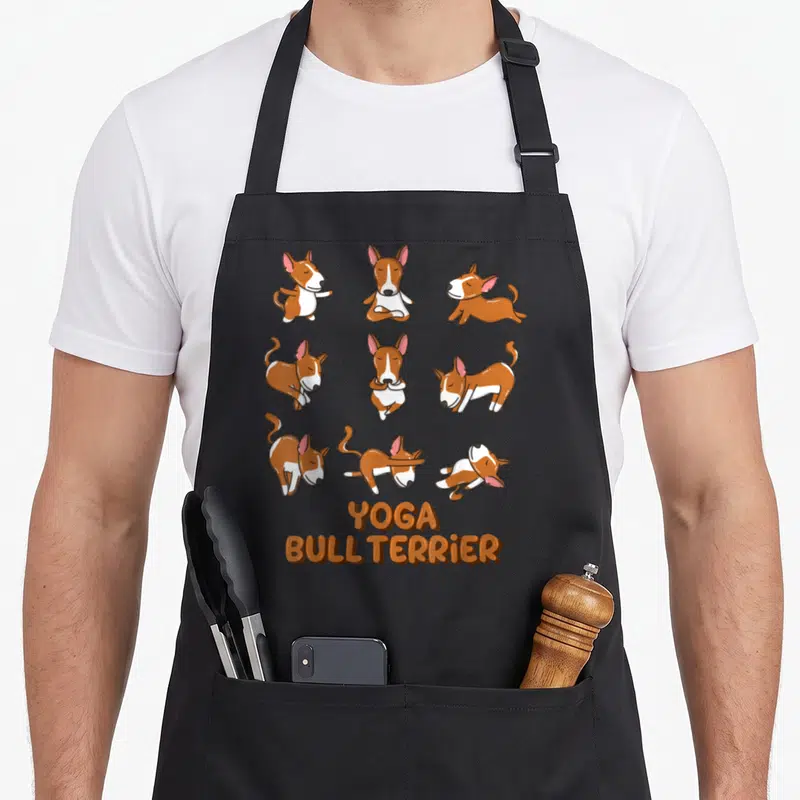 Tablier de cuisine noir avec neuf illustrations de Bull Terrier en poses de yoga et le texte Yoga Bull Terrier en orange.