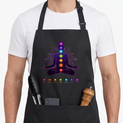 Tablier de cuisine noir avec silhouette assise en lotus et sept chakras colorés alignés verticalement sur le dos.