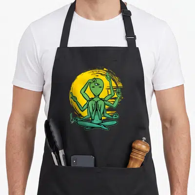 Tablier de cuisine noir avec alien vert à multiples bras en posture de yoga devant un cercle jaune.