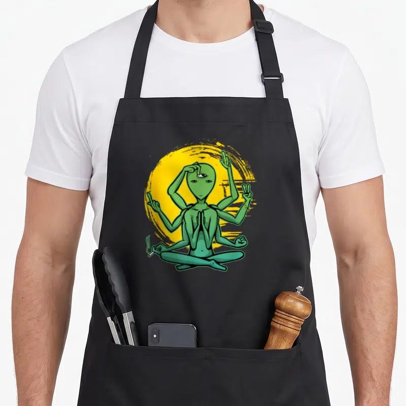 Tablier de cuisine noir avec alien vert à multiples bras en posture de yoga devant un cercle jaune.