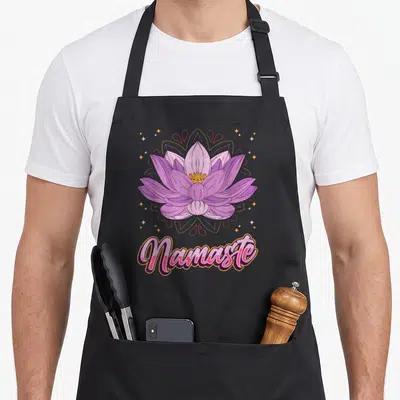 Tablier de cuisine noir avec une fleur de lotus rose et le mot Namaste en calligraphie colorée.