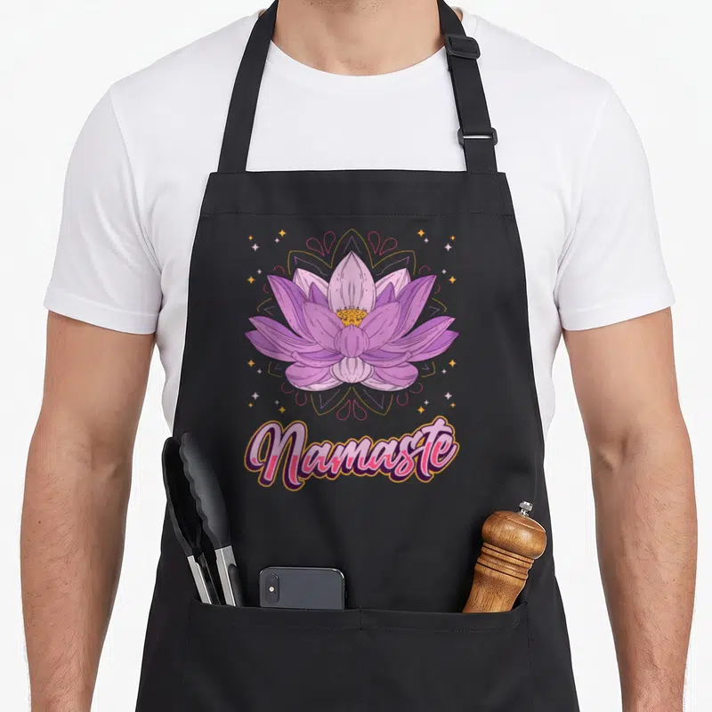Tablier de cuisine noir avec une fleur de lotus rose et le mot Namaste en calligraphie colorée.