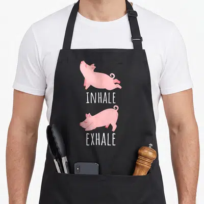 Tablier de cuisine noir avec un cochon rose illustrant les mouvements d'inspiration et d'expiration.