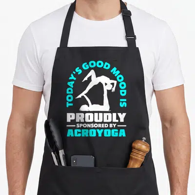 Tablier de cuisine noir avec illustration acroyoga et texte en turquoise et blanc sur fond uni.