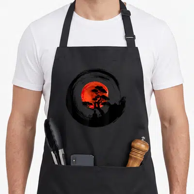 Tablier de cuisine noir avec cercle Enso, soleil rouge, arbre bonsaï et silhouette de Boudda assis.